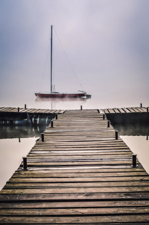 Foggy morning on the lake. Boat and wooden pier at Lake Parpocany in Tychy, Poland.の写真素材