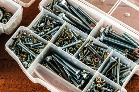 Silver and gold metal screws. Bolts and screws in plastic container.の写真素材