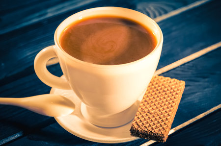 Coffee and cake in vintage style. Coffee with waffle on a navy blue wooden table. Photo with a shallow depth of field.の写真素材
