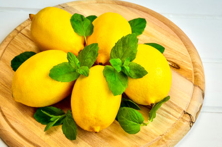 Yellow fruits with green leaves on a wooden board. Lemons with mint leaves on a chopping board.の写真素材