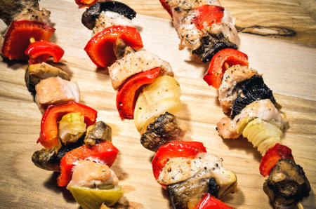 Concept with tasty grilled food. Skewers of meat with turkey, red peppers, mushrooms and onions on a chopping board.の写真素材