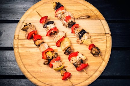 Concept with tasty grilled food. Skewers of meat with turkey, red peppers, mushrooms and onions on a chopping board.の写真素材