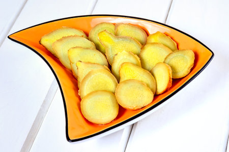 Concept with fresh herbs. Slices of ginger in a bowl on a wooden white table.の写真素材
