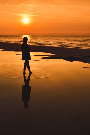 Woman on the seashore in a beautiful evening scenery. Girl walking on the beach with the setting sun in the background. Photo taken at the Baltic Sea in Leba, Poland.の写真素材