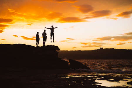 Three people on sunset. Beautiful jump on sunset. Silhouette on the sky. Orange sunset. Malta. Sea view.の写真素材