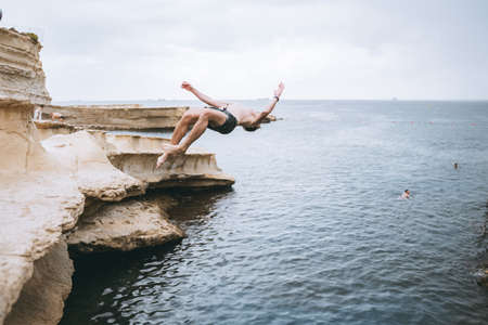 A man swimming in a body of water. Jumping from rock to the water with saltoの写真素材