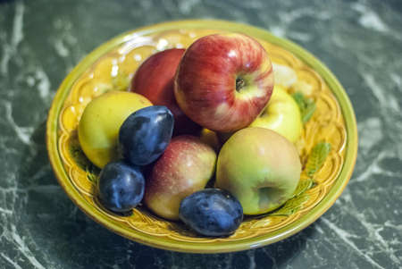 Apples and plums in a deep vase
