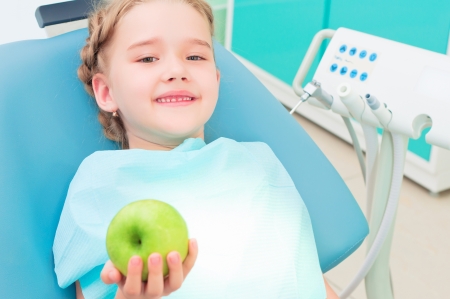 girl in the dentist s chair shows a green apple, regular care of your teethの写真素材