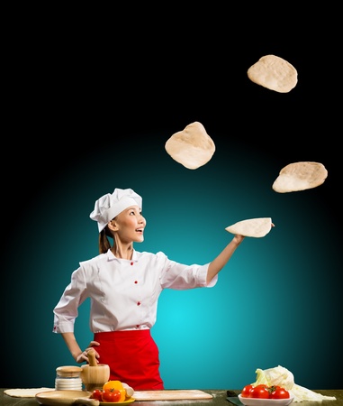 Asian woman chef juggling with pieces of dough for pizzaの写真素材