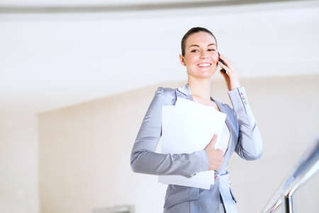 Portrait of a successful business woman in the office, holding papers and talking on cell phoneの写真素材