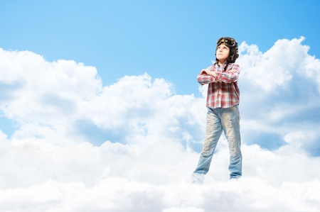 Boy in helmet pilot stands with his arms crossed in the clouds, dreaming of becoming a pilotの写真素材