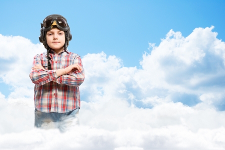 Boy in helmet pilot stands with his arms crossed in the clouds, dreaming of becoming a pilotの写真素材