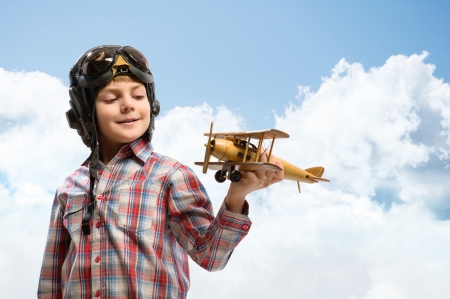 Boy in helmet pilot playing with a toy wooden airplane in the clouds, dreaming of becoming a pilotの写真素材