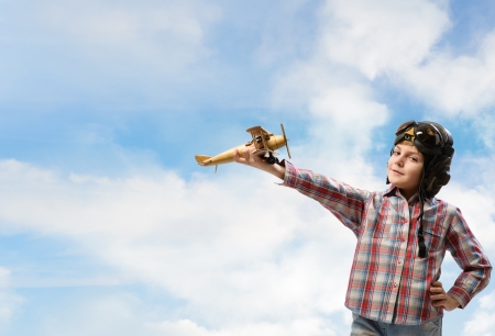 Boy in helmet pilot playing with a toy wooden airplane in the clouds, dreaming of becoming a pilotの写真素材
