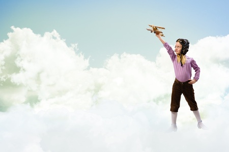 girl in helmet pilot playing with a toy wooden airplane in the clouds, dreaming of becoming a pilotの写真素材