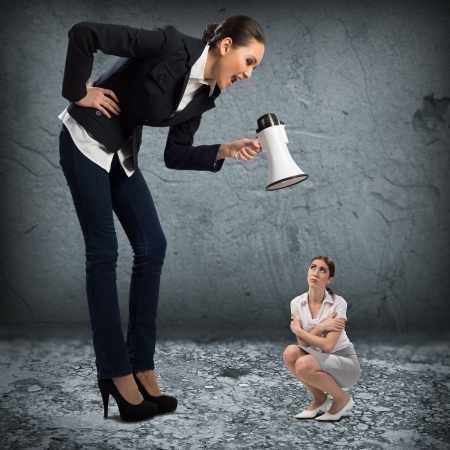 Business woman yelling at a small woman sitting on the ground, the concept of aggressionの写真素材