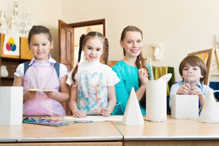 children with the teacher standing at the table, smiling and looking into the camの写真素材