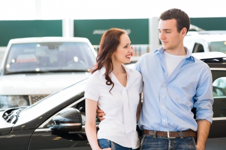 Young couple standing embracing near a car in the showroomの写真素材