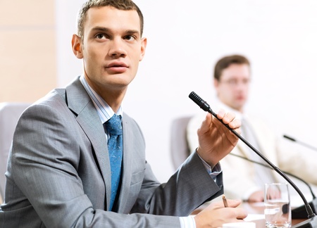 Portrait of a businessman, said into the microphone, in the background colleagues communicate with each otherの写真素材