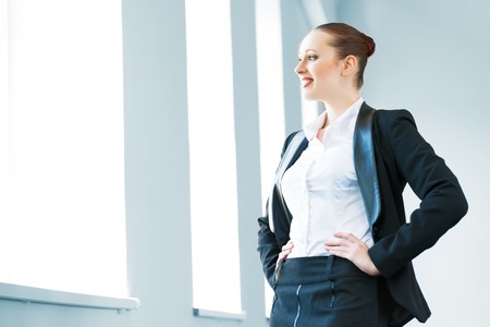 young modern business woman in a bright office smiling and looking out the windowの写真素材