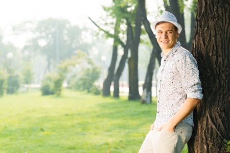 portrait of a young man, stands leaning against a tree in a summer parkの写真素材