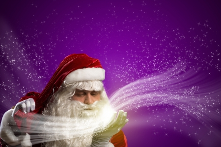 santa claus blows with hands magic sparks holds on shoulder bag with Christmas presentsの写真素材