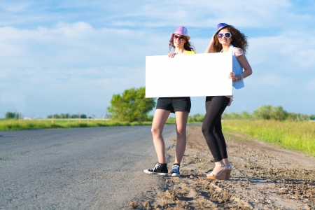 Two young women stand with a blank banner on the side of the road, place for textの写真素材
