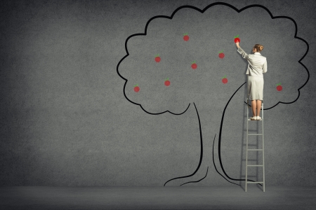 business woman standing on a ladder and touches of tree painted on the wallの写真素材