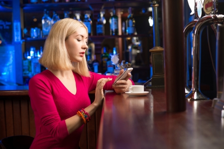 portrait of a young woman in a bar with a cell phone and a cup of coffeeの写真素材