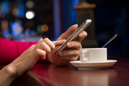 close-up of female hands holding a cell phone, sitting at the bar, next to a cup of coffeeの写真素材
