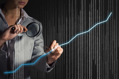 business woman draws a graph with a magnifying glass on the screen tich binary codeの写真素材