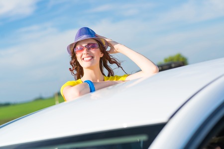 young woman got out of the car window, holds the hand hat and laughing