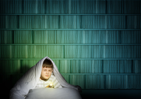 image of a frightened boy under the covers with a flashlightの写真素材