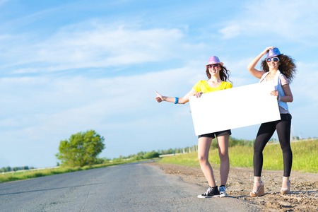 Two young women stand with a blank banner on the side of the road, place for textの写真素材