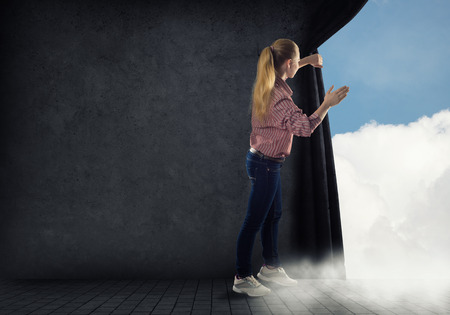 young woman pushes the curtain looking at cloudsの写真素材