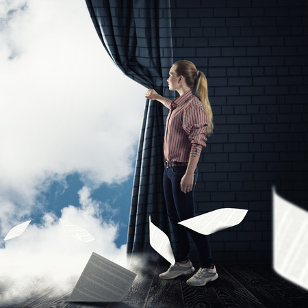image of a young woman pushes the curtain looking at cloudsの写真素材