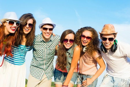 group of young people wearing sunglasses and hats hugging and standing in a row, spending time with friendsの写真素材