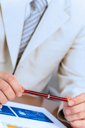 businessman holding a pen in hand, in front of him laid paper business financial chartsの写真素材
