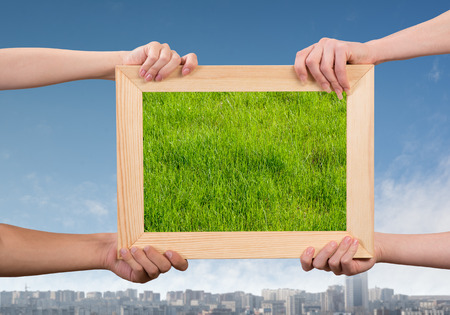 Close up of human hands holding wooden frame with green grassの写真素材