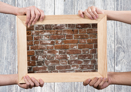 Close up of human hands holding wooden frame with brick textureの写真素材