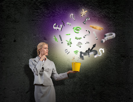 Young businesswoman holding bucket with currency signs flying outの写真素材
