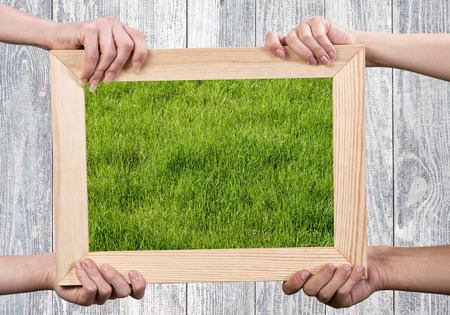 Close up of human hands holding wooden frame with green grassの写真素材
