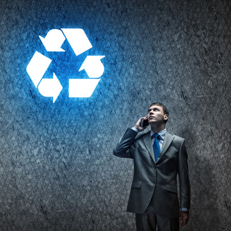 Young thoughtful businessman looking up a recycing symbolの写真素材