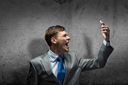 Young businessman screaming furiously in mobile phoneの写真素材