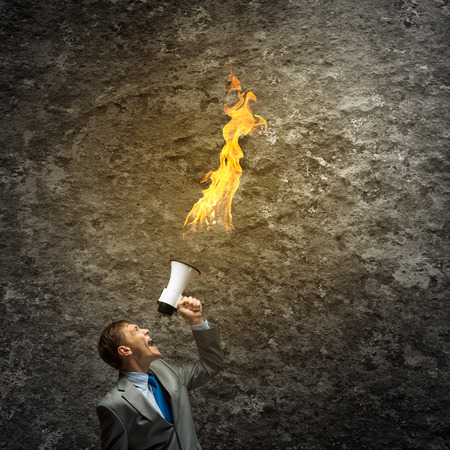 Young aggressive businessman screaming furiously in megaphoneの写真素材