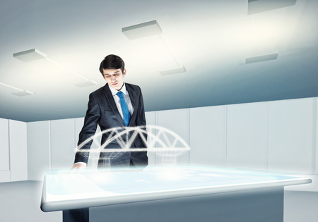 Young businessman looking at hologram of construction projectの写真素材