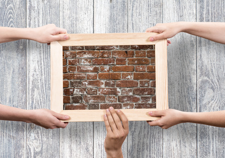 Close up of human hands holding wooden frame with brick textureの写真素材