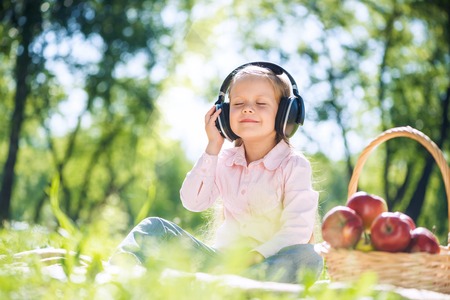 Little cute girl in summer park listening musicの写真素材