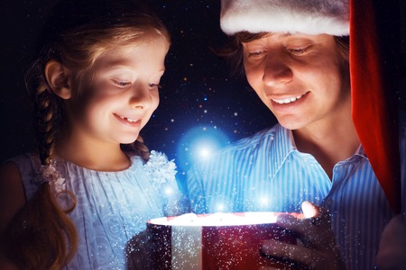 father in Santa Claus cap and daughter opened a box with Christmas gift boxes of shining light and magicの写真素材