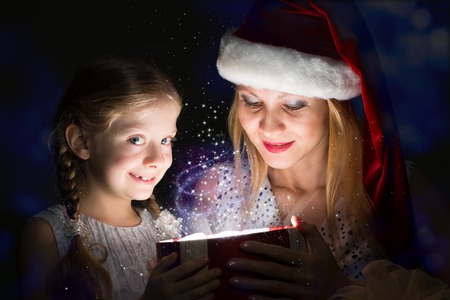 mother in Santa Claus cap and daughter opened a box with Christmas gift boxes of shining light and magicの写真素材